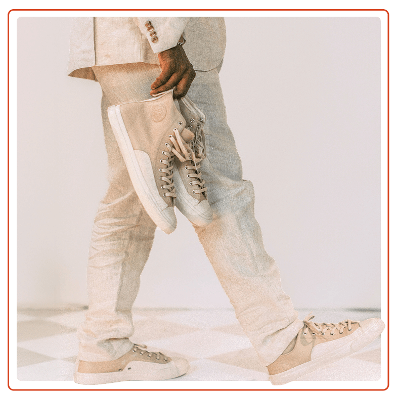 Person holding taupe high-top sneakers while wearing a neutral suit with low-top sneakers.