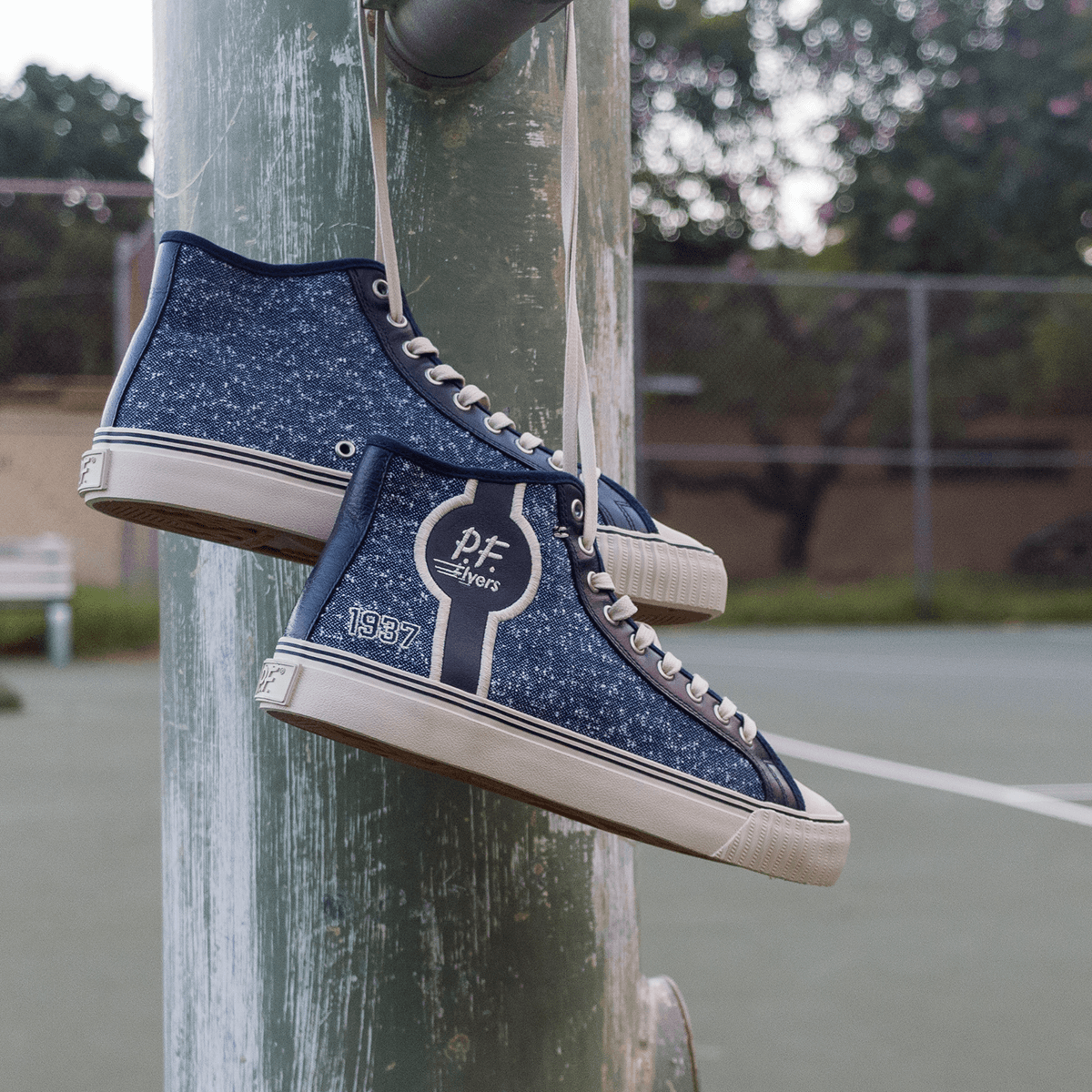 Navy high-top sneakers with jersey-textured fabric and white soles dangling from a metal pole.