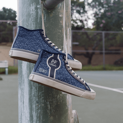 Navy high-top sneakers with jersey-textured fabric and white soles dangling from a metal pole.