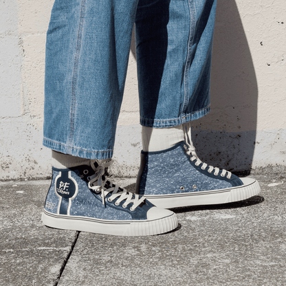 Navy jersey-textured high-top sneakers worn with jeans, standing against a concrete wall.