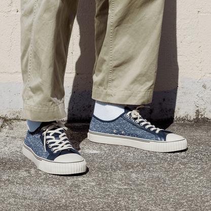 Navy jersey-textured low-top sneakers worn with khaki pants, standing against a concrete wall.