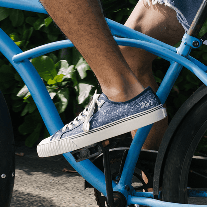 Person wearing navy sneakers with white soles on a blue bicycle.
