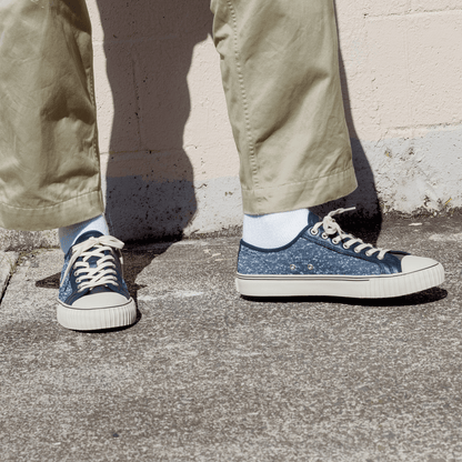 Navy jersey-textured low-top sneakers worn with khaki pants, standing against a concrete wall.
