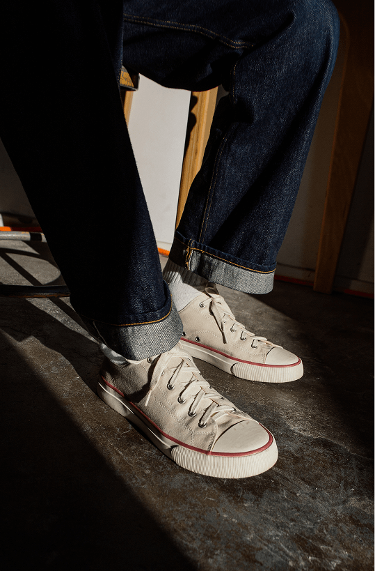 Person sitting on a chair wearing retro white sneakers with a crimson red accent and blue jeans.