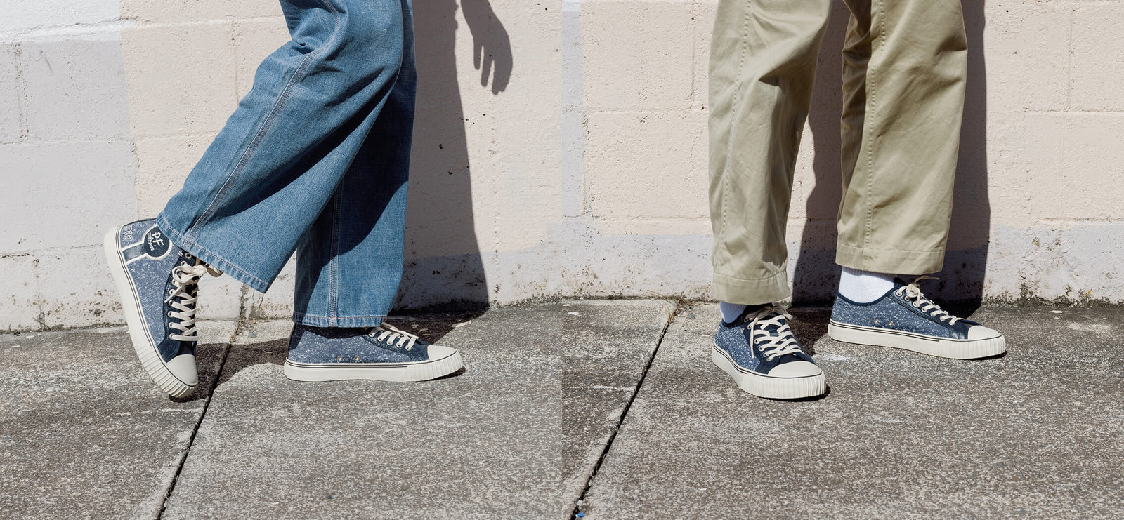 Two pairs of legs in blue jeans and navy sneakers standing on a sidewalk.