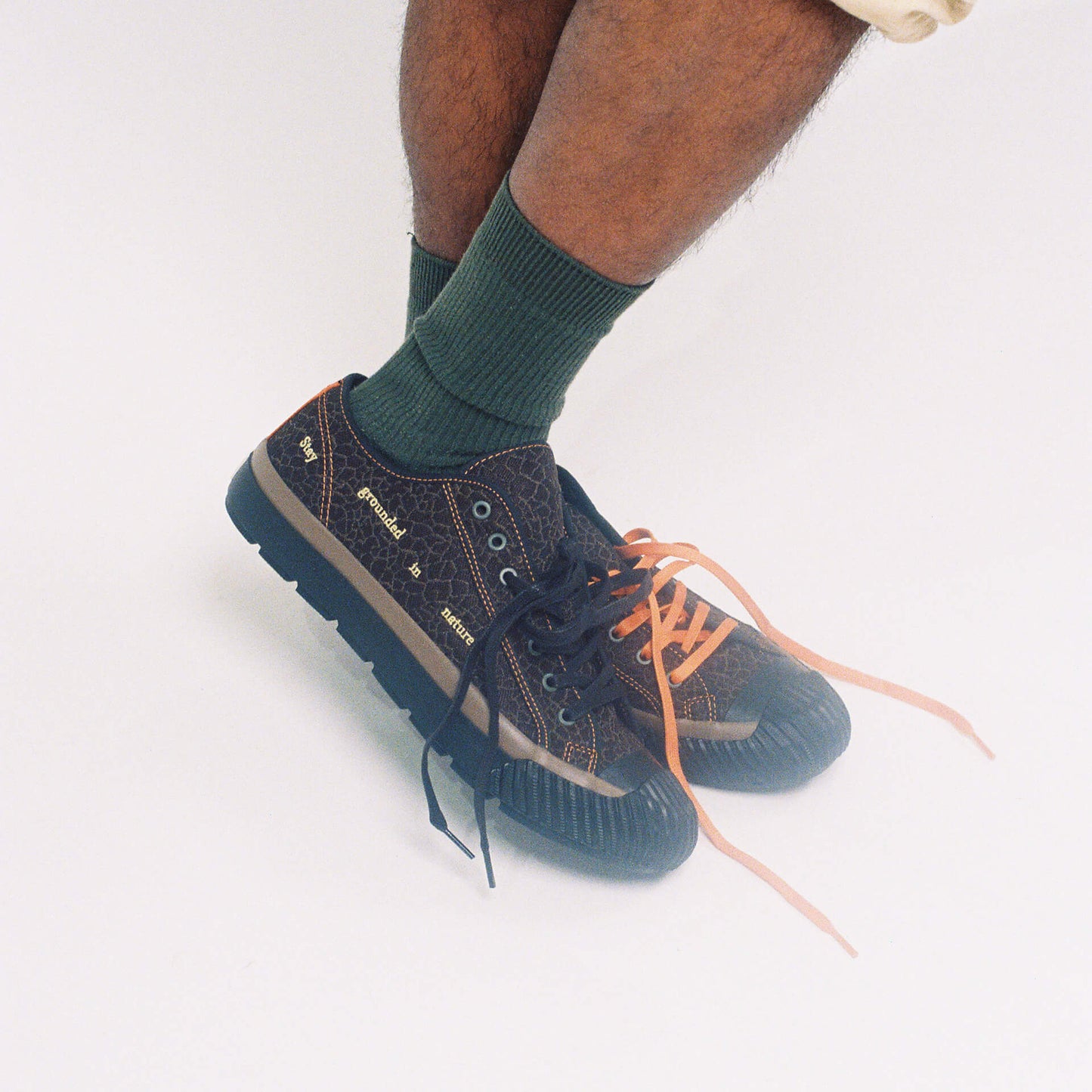 Person wearing brown low-top sneakers with black and orange laces on a white background.