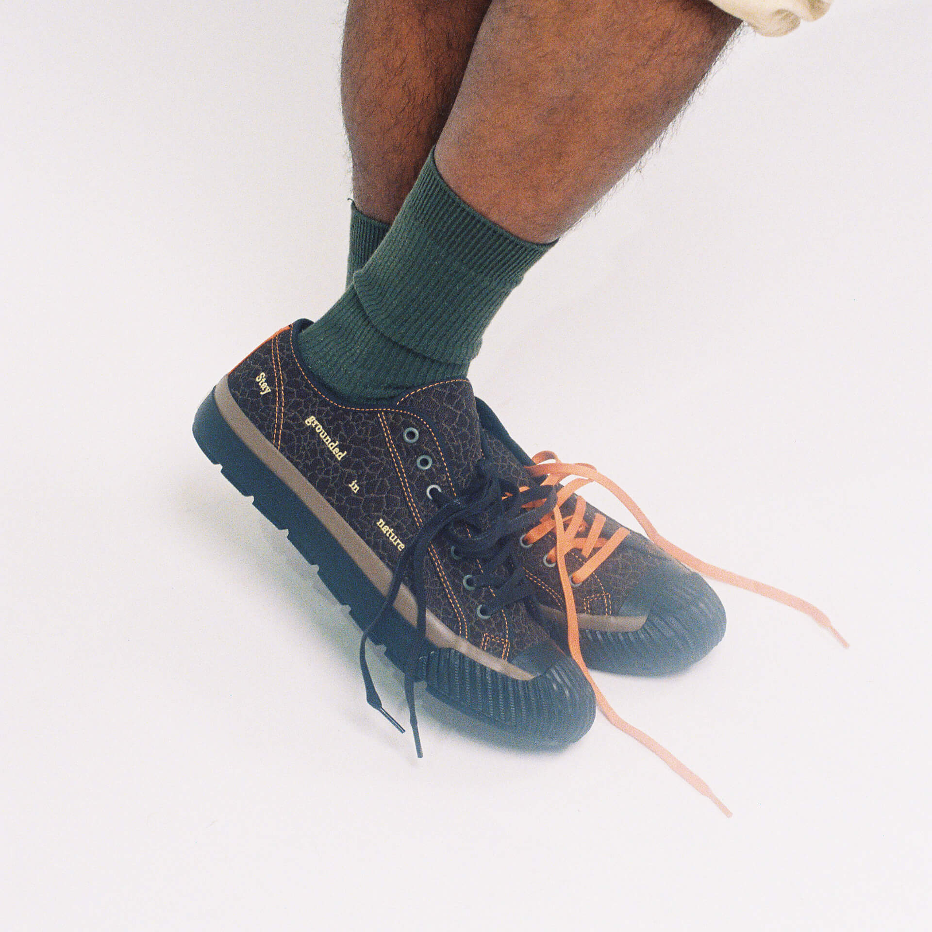 Person wearing brown low-top sneakers with black and orange laces on a white background.