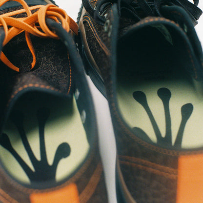Pair of brown low-top sneakers with frog footprint designs on the soles.