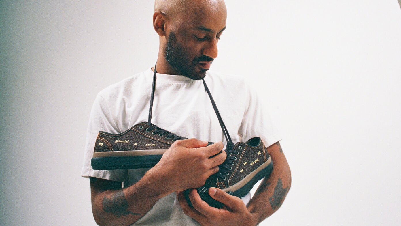 Man holding a pair of brown low-top sneakers against a plain background.