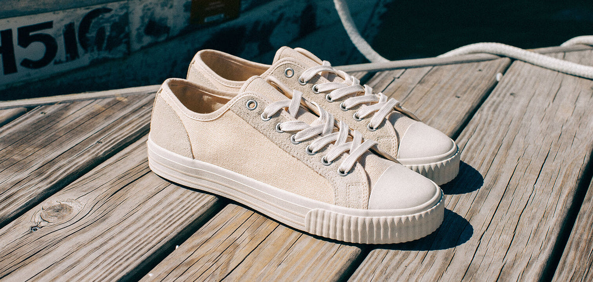 Pair of light cream low-top canvas sneakers resting on a wooden dock.