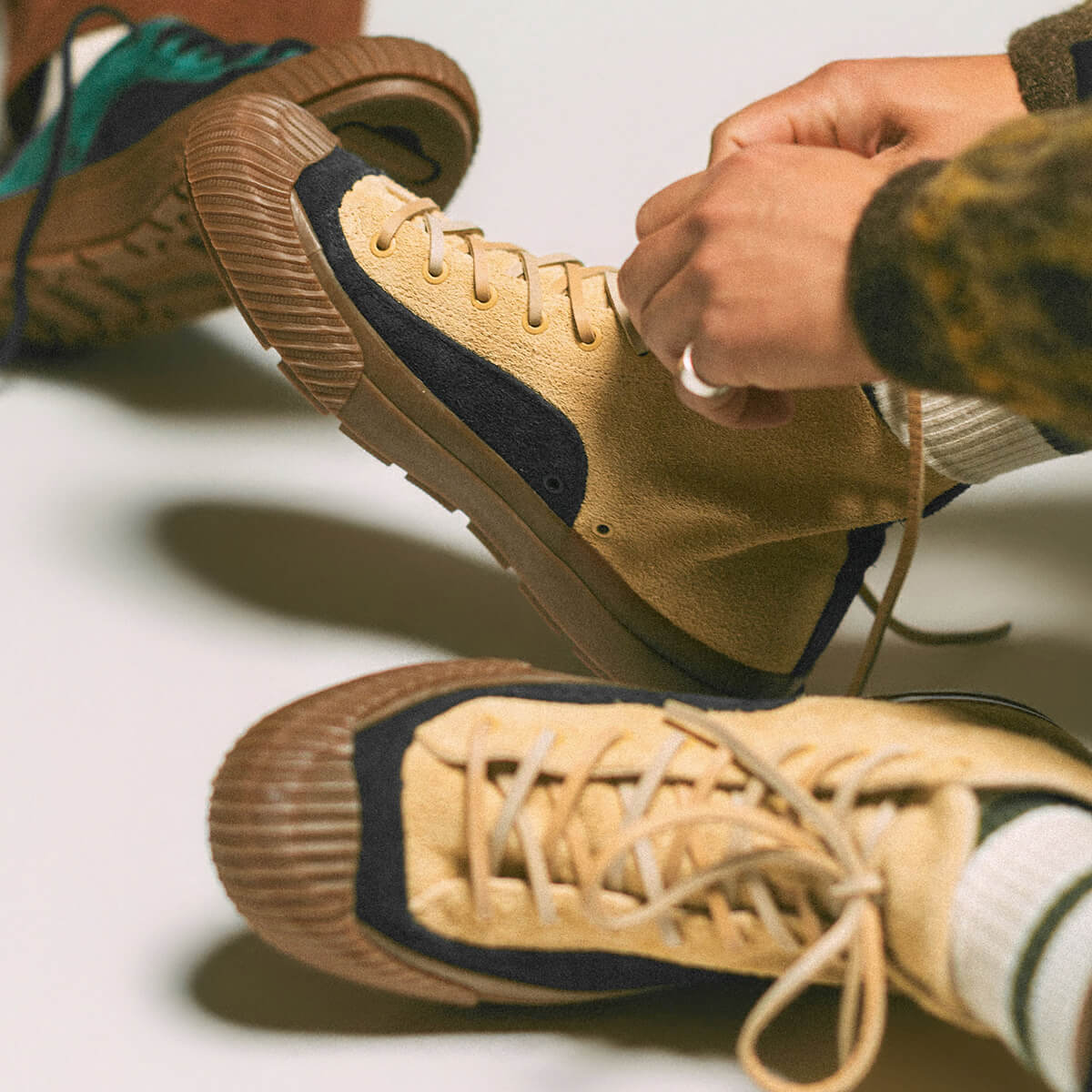 Person tying tan sneakers with black accents on a light background