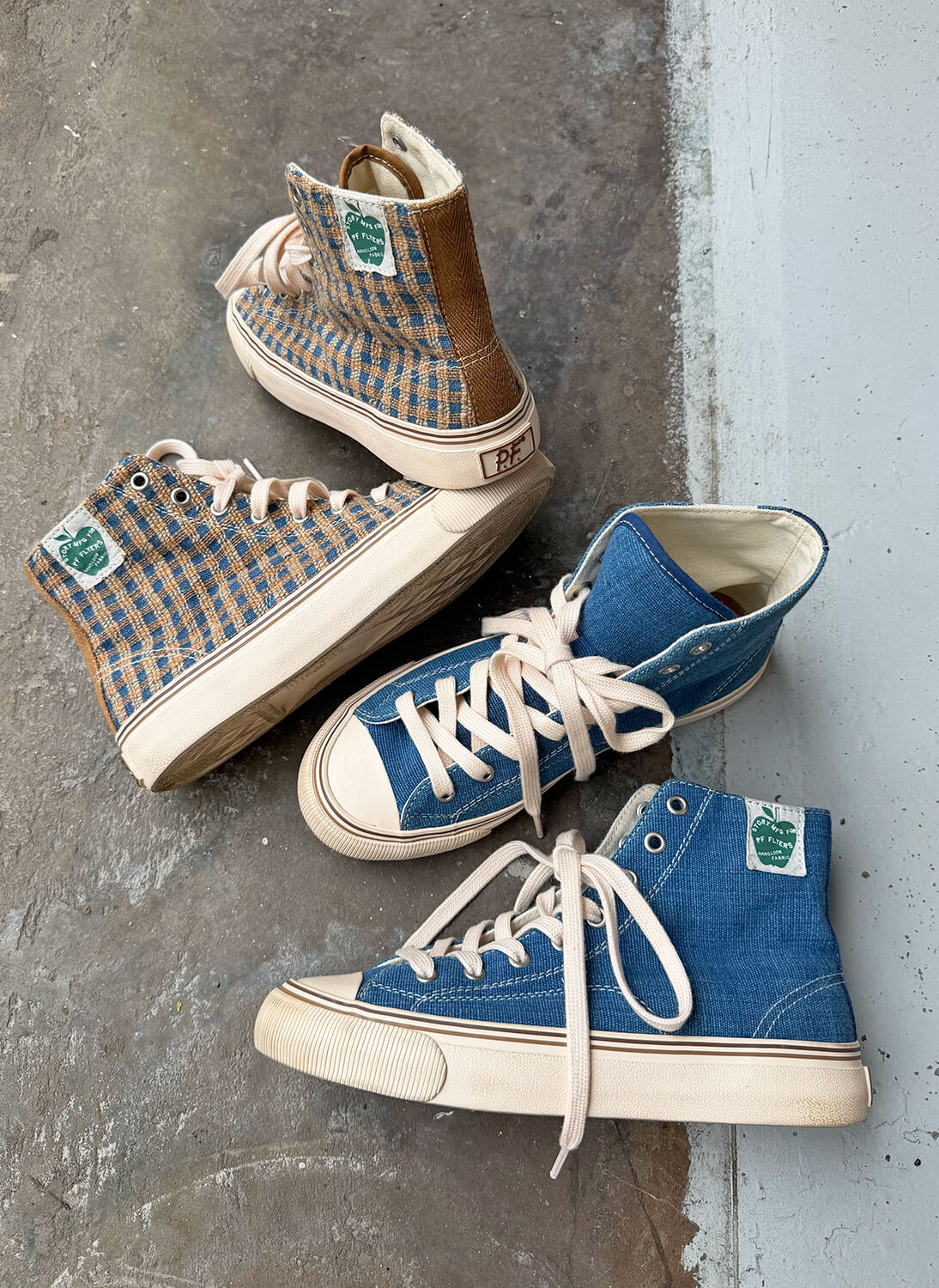 Two pairs of high-top sneakers with hand-woven fabric arranged on a concrete floor.