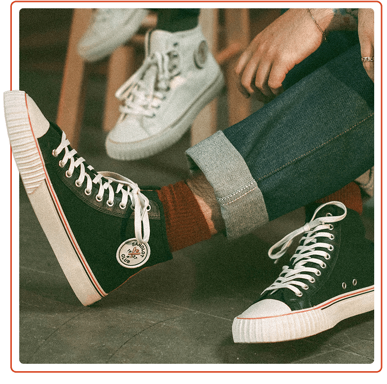 Person wearing black high-top sneakers with white laces on a wooden floor.