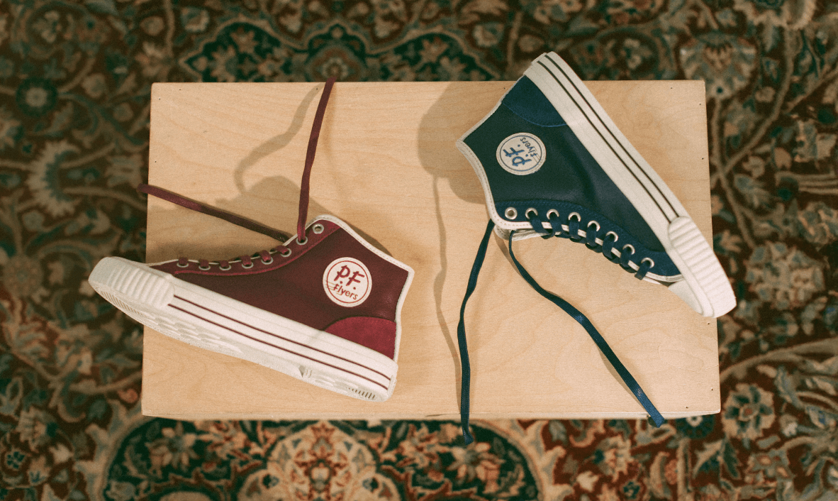 Two high-top sneakers, one burgundy and one blue, on a wood box with a patterned rug background.