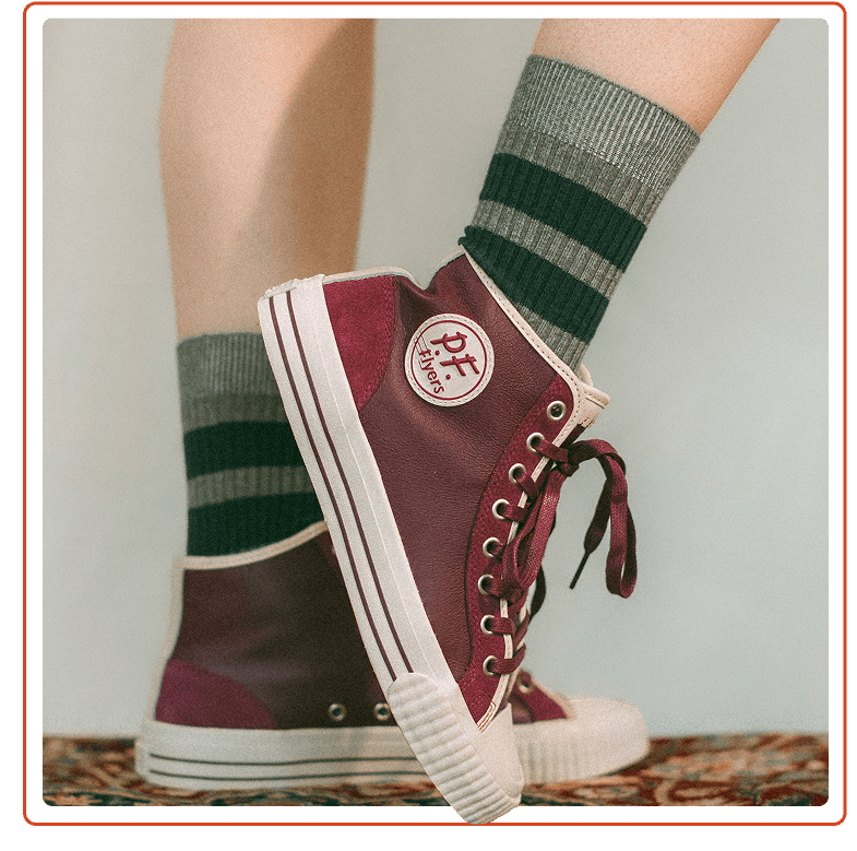 Burgundy high-top sneakers worn with green striped socks on a neutral background